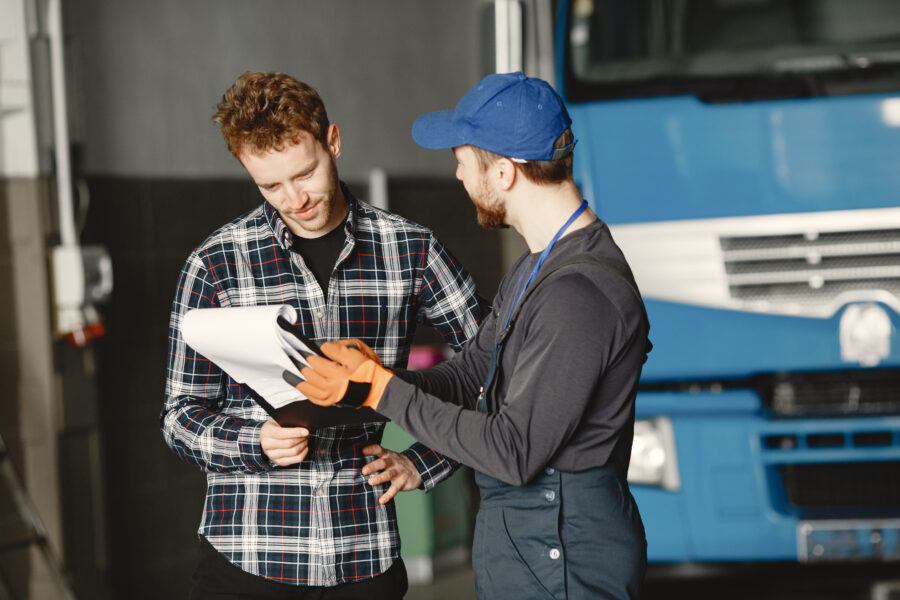 Two mechanics discussing the service checklist in front of a blue heavy-duty truck, emphasizing how often should a truck be serviced.